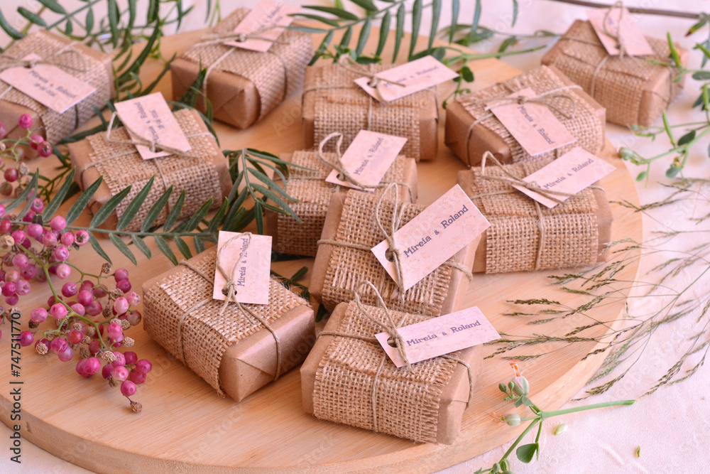 Autumn fall wedding decoration guest gifts rustic style soaps wrapped in brown craft paper jute fabric ribbon and custom labels with names, wodden table background with red berries and green leaves Autumn fall wedding decoration guest gifts rustic style soaps wrapped in brown craft paper jute fabric ribbon and custom labels with names, wodden table background with red berries and green leaves
