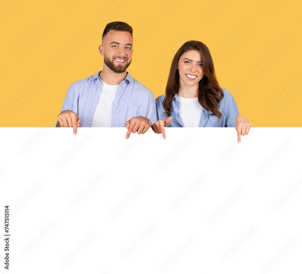 Smiling pair in denim pointing down at blank banner Smiling pair in denim pointing down at blank banner