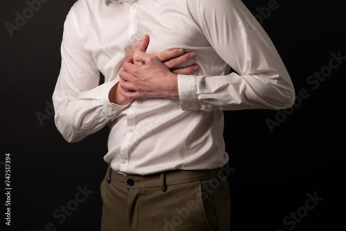 young man in formal office clothes having chest pain, and holdign two hands on chest.
