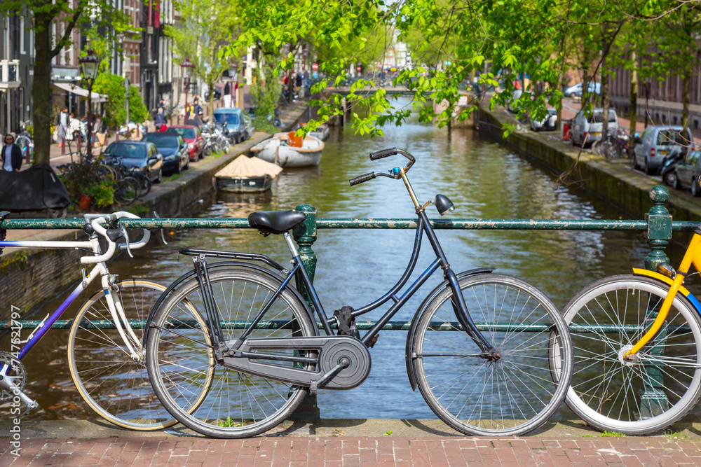Bicycles on the bridge in Amsterdam, Netherlands against a canal and old buildings during summer sunny day. Amsterdam postcard iconic view. Tourism concept.