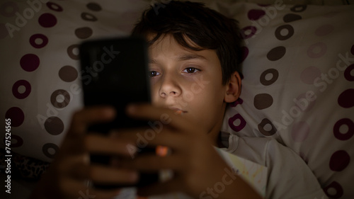 Fotografía Child addicted to smartphone browsing social media lying in bed suffering from insomnia and addicted