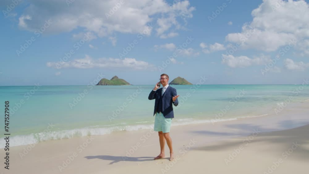 Successful young businessman friendly communcating on mobile phone standing barefoot on white sand, azure waters of the ocean washing his feet on the beach. High quality 4k footage Successful young businessman friendly communcating on mobile phone standing barefoot on white sand, azure waters of the ocean washing his feet on the beach. High quality 4k footage