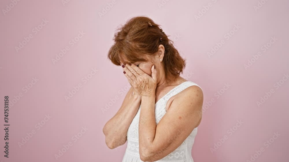 Stressed middle age woman in a dress standing isolated, covering her tear-stained face with hands. an image of sadness, depression over pink background. Stressed middle age woman in a dress standing isolated, covering her tear-stained face with hands. an image of sadness, depression over pink background.