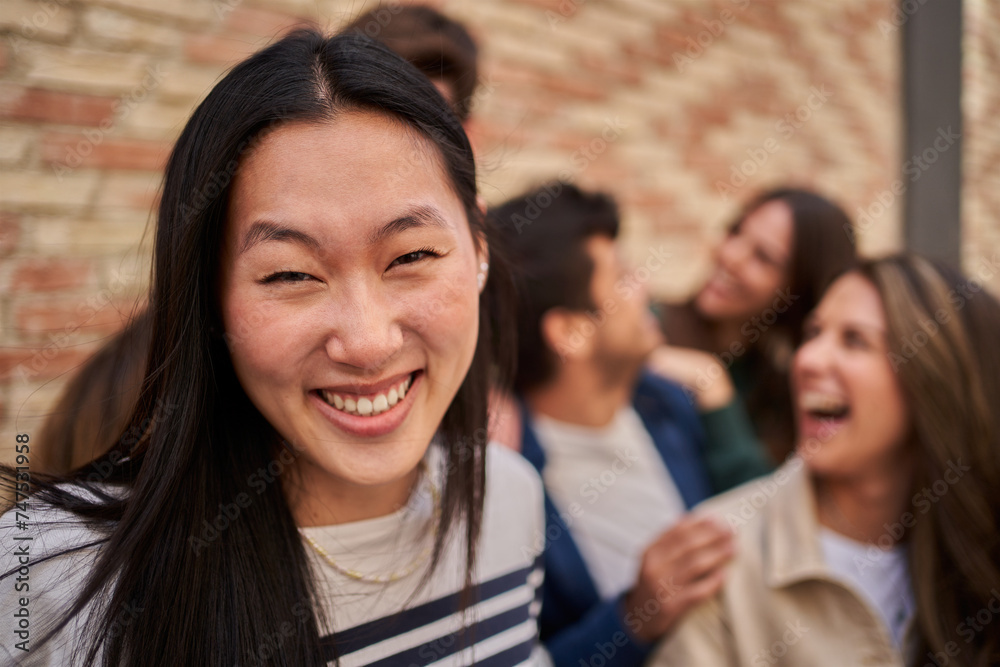 An Asian woman is happily smiling in front of a group of people at a leisure event. Chinese girl sharing a moment of fun and laughter, wearing stylish eyewear. Group of friends at the background