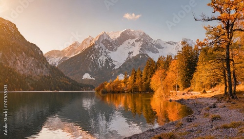 Mountain autumn landscape, tall fir trees on the shore of a lake with blue water, high mountains covered with snow