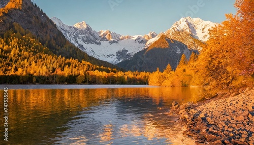 Mountain autumn landscape, tall fir trees on the shore of a lake with blue water, high mountains covered with snow