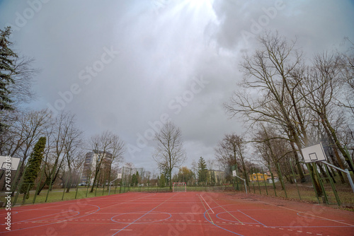 Boisko do piłki nożnej i koszykówki pod spektakularnie pochmurnym niebem. Boisko sportowe wśród starych drzew pod mocno zachmurzonym niebem w deszczowy styczniowy dzień.