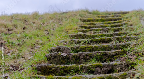 Stare malownicze betonowe schody na trawiastym wzgórzu.Zniszczone betonowe schody wspinające się po zboczu wzgórza w stronę pochmurnego nieba.