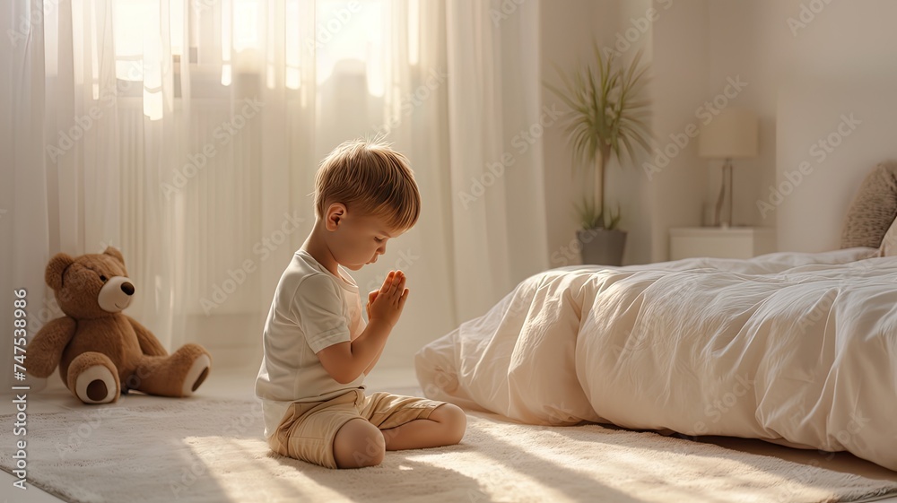 a three-year-old boy kneeling in prayer beside his bed in his bedroom, head bowed, with a teddy bear nearby, against a backdrop of soft white pastel colors. a three-year-old boy kneeling in prayer beside his bed in his bedroom, head bowed, with a teddy bear nearby, against a backdrop of soft white pastel colors.
