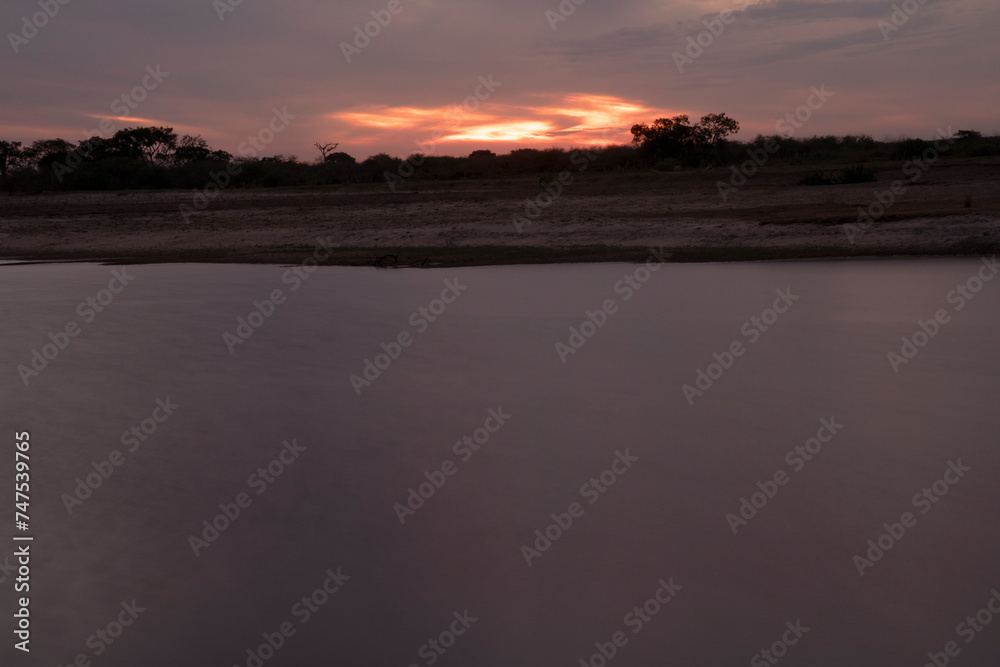 Long exposure shot of Corriente river in Esquina, Corrientes, Argentina, at sunset. Beautiful blurred water effect, dramatic clouds and hiding sun at nightfall.	