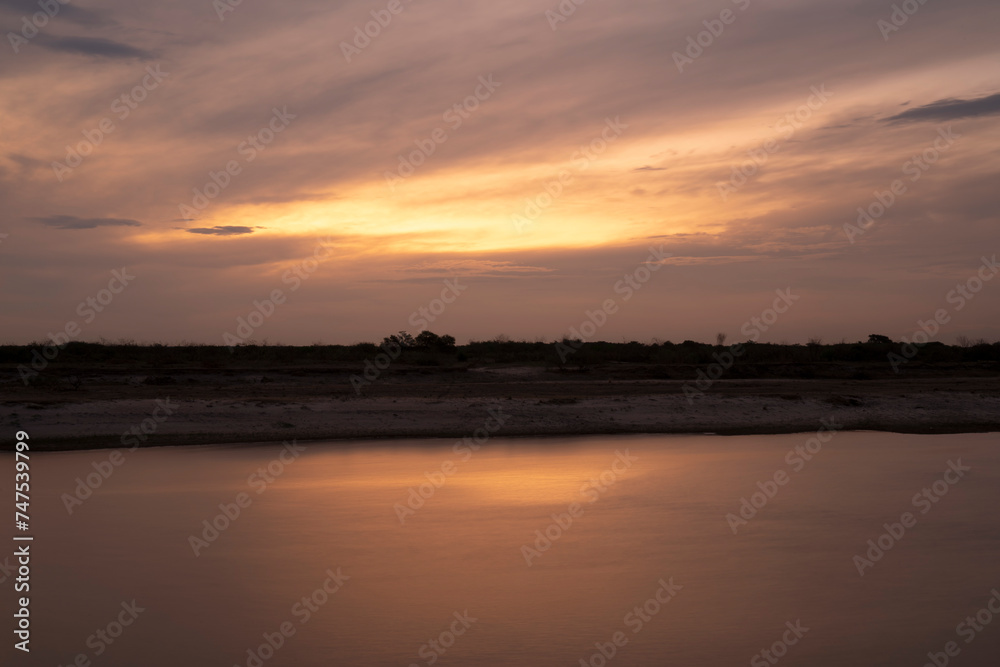 Long exposure shot of the river at nightfall. Panorama view of the river under a dramatic sunset sky. Beautiful sunlight and clouds reflection in the water surface.