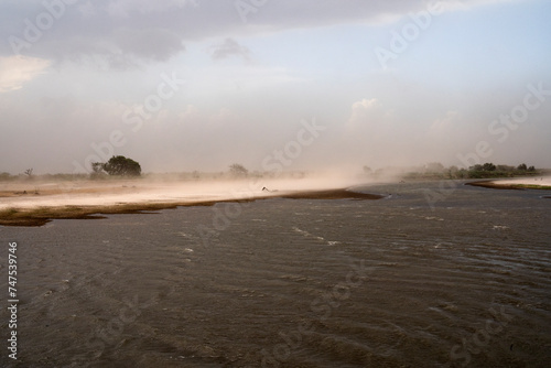Panorama view of the river and beach under a wind storm that raises the sand. 