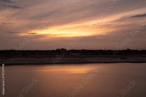 Long exposure shot of the river at nightfall. Panorama view of the river under a dramatic sunset sky. Beautiful sunlight and clouds reflection in the water surface. © Gonzalo
