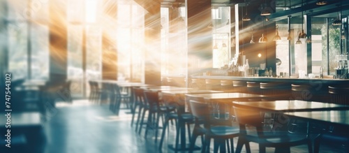 The image shows a blurred interior of a modern cafe  with various tables and chairs scattered around. The lack of focus creates a sense of movement and activity within the restaurant.