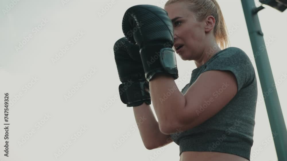Focused woman with boxing gloves training outdoors. Low angle view capturing her determination and strength. sport and fitness concept Focused woman with boxing gloves training outdoors. Low angle view capturing her determination and strength. sport and fitness concept