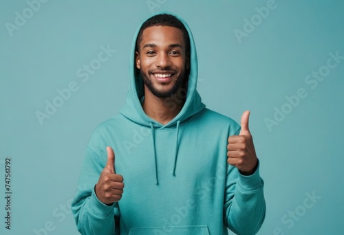 A casual man in a teal hoodie gives double thumbs up, his smile exuding friendliness and approachability. photo