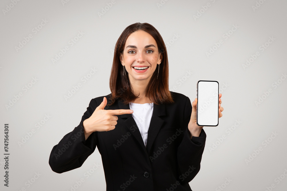 Enthusiastic businesswoman in a sleek black suit happily presenting a smartphone with a blank screen Enthusiastic businesswoman in a sleek black suit happily presenting a smartphone with a blank screen