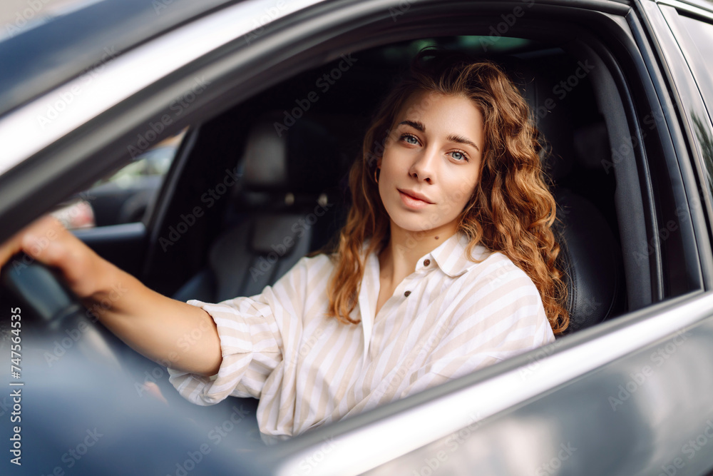 Female driver. Portrait of young beautiful woman in  sweater sitting in the car. Car travel, tourism, carshering concept.