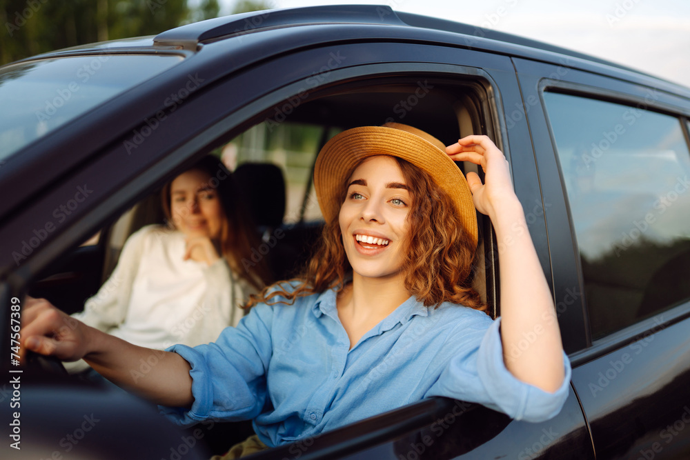 Two trendy attractive young woman singing along to the music as they drive along in the car through town. Beautiful female friends in the car enjoy a car trip together. Two trendy attractive young woman singing along to the music as they drive along in the car through town. Beautiful female friends in the car enjoy a car trip together.