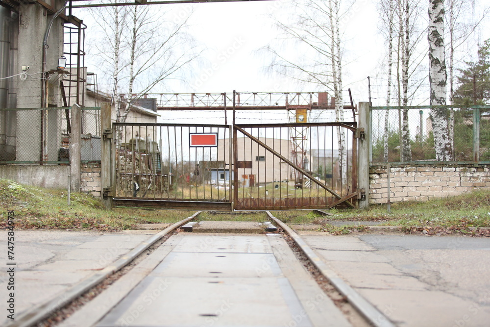 Naklejka premium Railway tracks run into the metal gate of the industrial zone of the plant