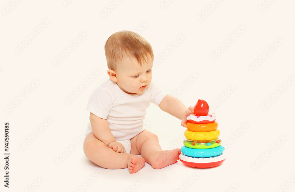 Happy little baby playing with toys sitting on floor on white studio background Happy little baby playing with toys sitting on floor on white studio background