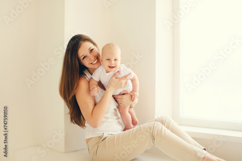 Happy smiling young mother playing with baby in white room at home