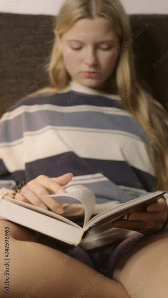 In the cozy atmosphere of the living room, a teenage girl sits on the sofa, alternately flipping through and reading the pages of a book. . Vertical In the cozy atmosphere of the living room, a teenage girl sits on the sofa, alternately flipping through and reading the pages of a book. . Vertical