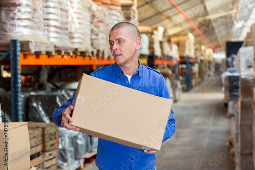 Caucasian man carrying cardboard box while working in warehouse.