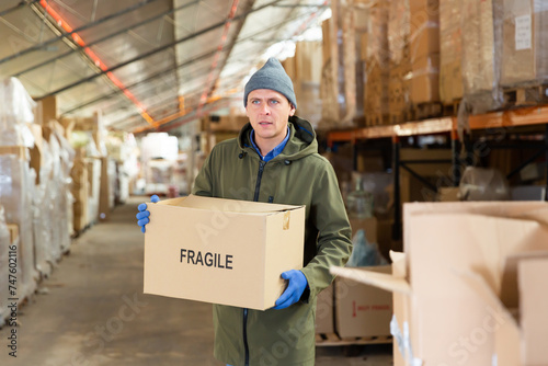 Warehouse worker carrying large box of goods in a warehouse