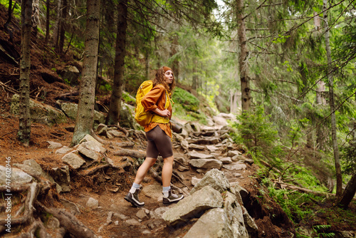 Beautiful traveling woman in the mountains on a background of a forest. Hiking, active lifestyle. Outdoor recreation concept.
