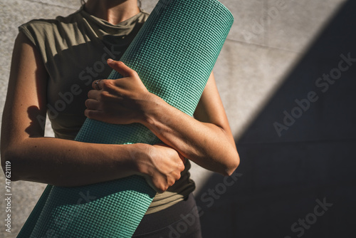 Fototapeta Naklejka Na Ścianę i Meble -  One caucasian woman hold yoga mat while stand outdoor in sunny day