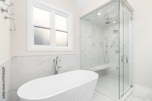 A bathroom s freestanding tub with a chrome faucet  marble tile on the walls and floor  and a walk-in shower with marble walls and bench. No brands or labels.