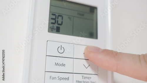 Close-up, the man turns on the air conditioner with the white remote control on the wall and increases the temperature.