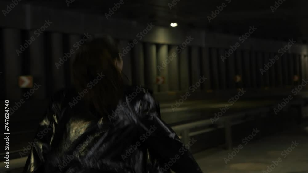 Asian woman walking and running against the background of an empty road at night. Lady in a black light coat under a bridge, rear view Asian woman walking and running against the background of an empty road at night. Lady in a black light coat under a bridge, rear view