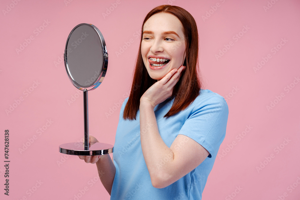Attractive ginger woman looking in mirror, winking, feeling satisfied with her teeth Attractive ginger woman looking in mirror, winking, feeling satisfied with her teeth
