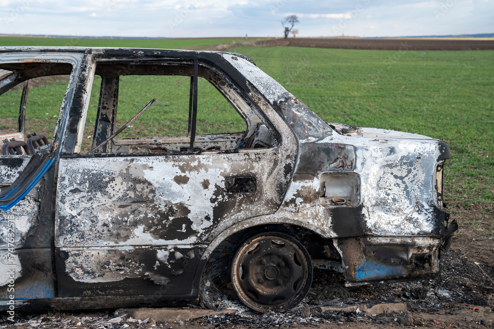 Fototapeta premium A burned out car. Burnt car in the field. Car fire, vehicle fire due to short circuit. Stolen car intentional arson. One vehicle was damaged in the fire.