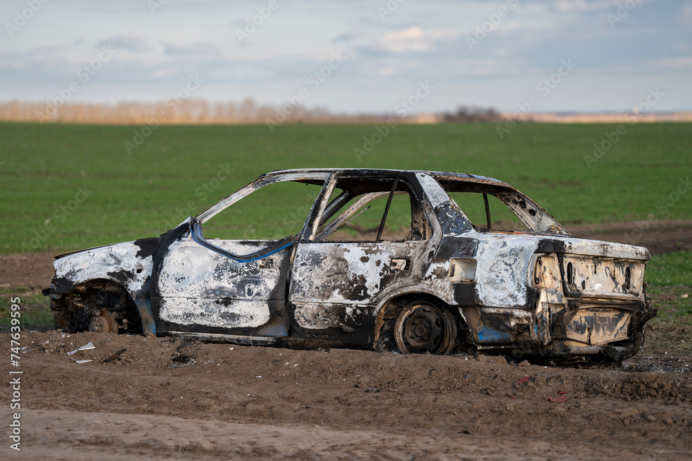 Fototapeta premium A burned out car. Burnt car in the field. Car fire, vehicle fire due to short circuit. Stolen car intentional arson. One vehicle was damaged in the fire.