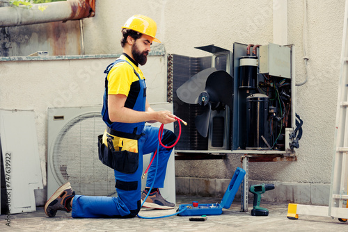 Skilled technician commissioned for routine air conditioner maintenance, assembling manometer before starting work. Trained engineer checking refrigerant leaks leading to reduced cooling efficiency