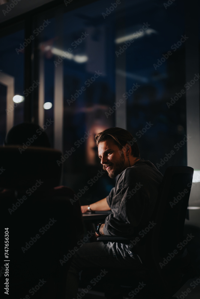 A young male professional is captured in a contemplative mood as he works overtime in a dimly lit, contemporary office setting.
