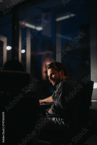 A young male professional is captured in a contemplative mood as he works overtime in a dimly lit, contemporary office setting.