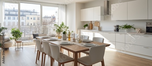 A contemporary white kitchen and dining room featuring a table and chairs neatly arranged near a window. The setting is clean, functional, and stylish.