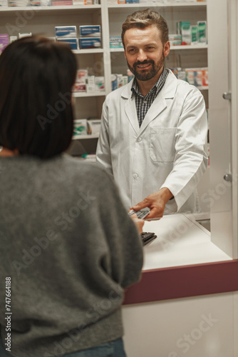 Professional male pharmacist selling medications at drugstore to a woman customer