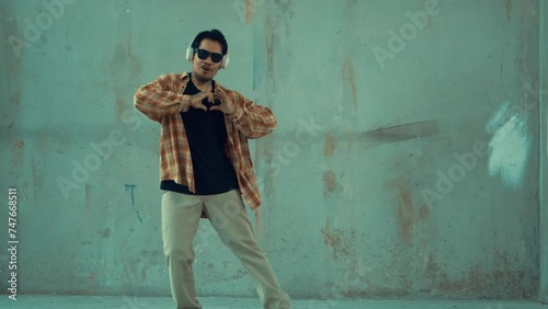 Attractive hispanic dancer in casual look practice street dance while listen music from headphone at cement background. Motion shot of break dancing performance. Outdoor sport 2024. hiphop.