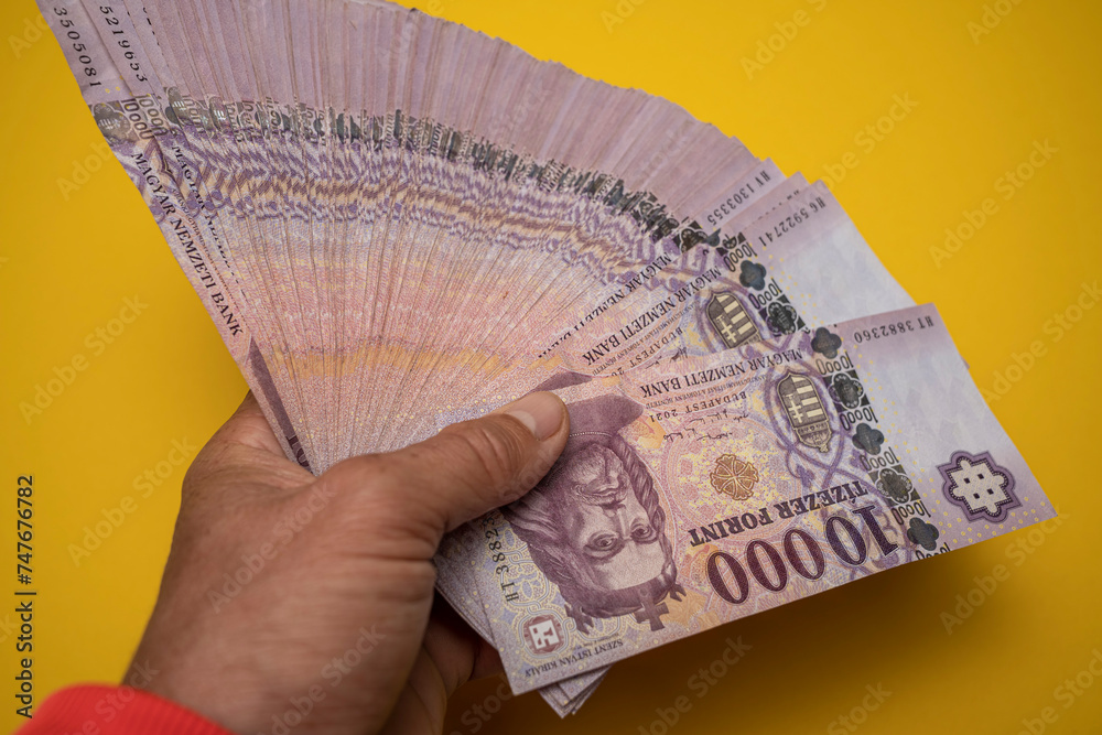 A man holds a stack of Hungarian paper forints in his hand. Against a yellow background. Concept showing the Hungarian economy.