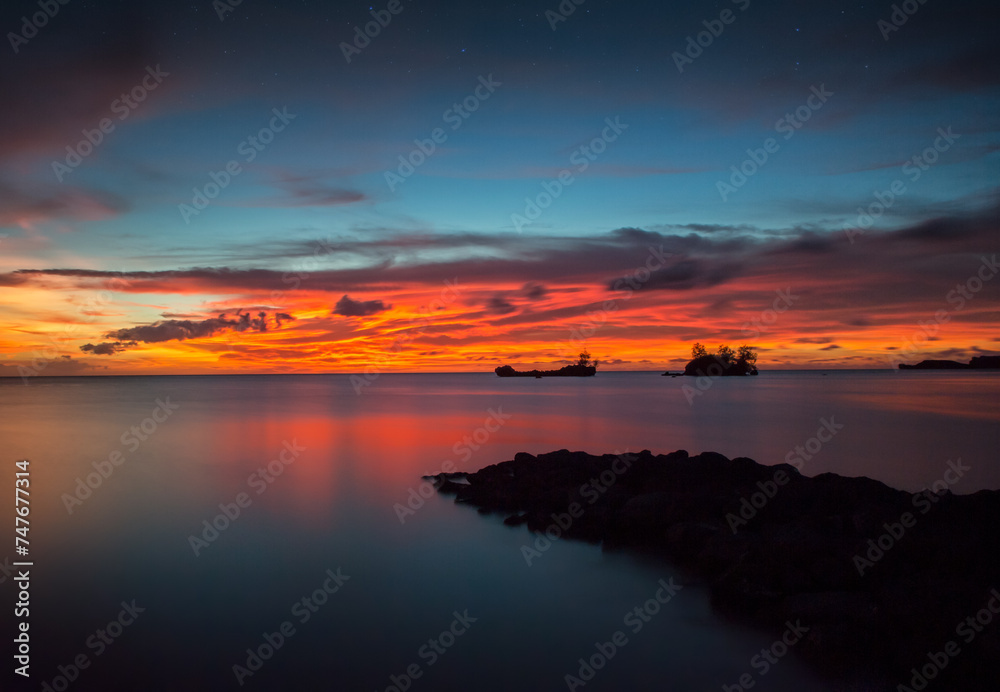 An ocean view of the sunset from Agat, Guam with a breakwater in the foreground