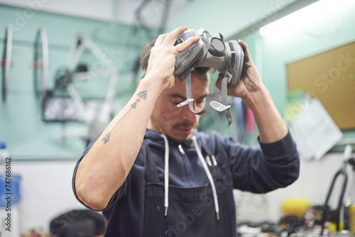 Photography Portrait of an hispanic young worker removing a respiratory protection mask, as he finishes a spray painting job in his workshop