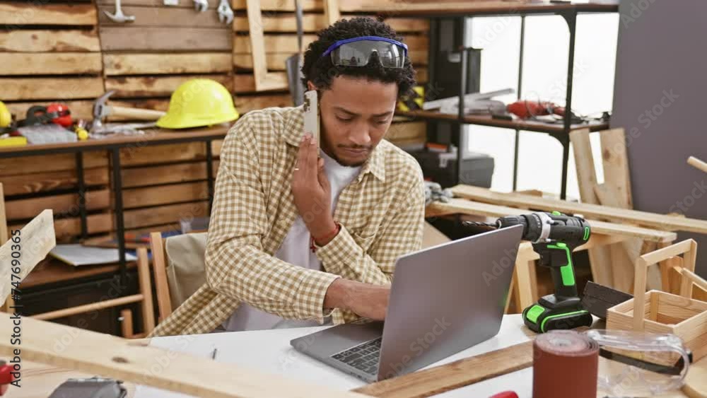 Handsome young man multitasking with a phone and laptop in a workshop Handsome young man multitasking with a phone and laptop in a workshop