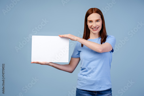 Redhead beauty in a T shirt, showing an empty board, isolated on a blue background. Mockup concept