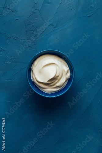 Yogurt is presented in a blue bowl on a blue background, captured from an aerial view, showcasing smooth curves, rustic simplicity, and an ivory color.