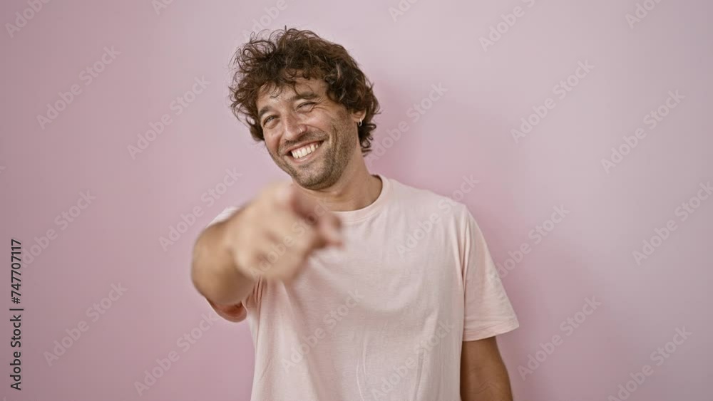 A cheerful young man pointing and smiling against a pink background exudes confidence and joy.